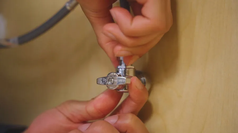 Hand turning an under-sink shutoff valve during faucet service for Faucet Repair & Replacement in Lakewood, CA